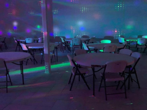 A disco ball reflecting colorful light beams throughout a room with tables and chairs set up for an event